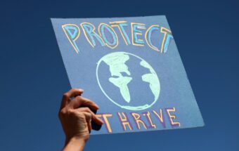 Harmony Cummings holds a sign outside the office of Senator John Hickenlooper (D-CO) during a Time to Thrive rally organized by the Colorado Green New Deal coalition to demand support for the THRIVE act on March 31, 2021, in Denver.