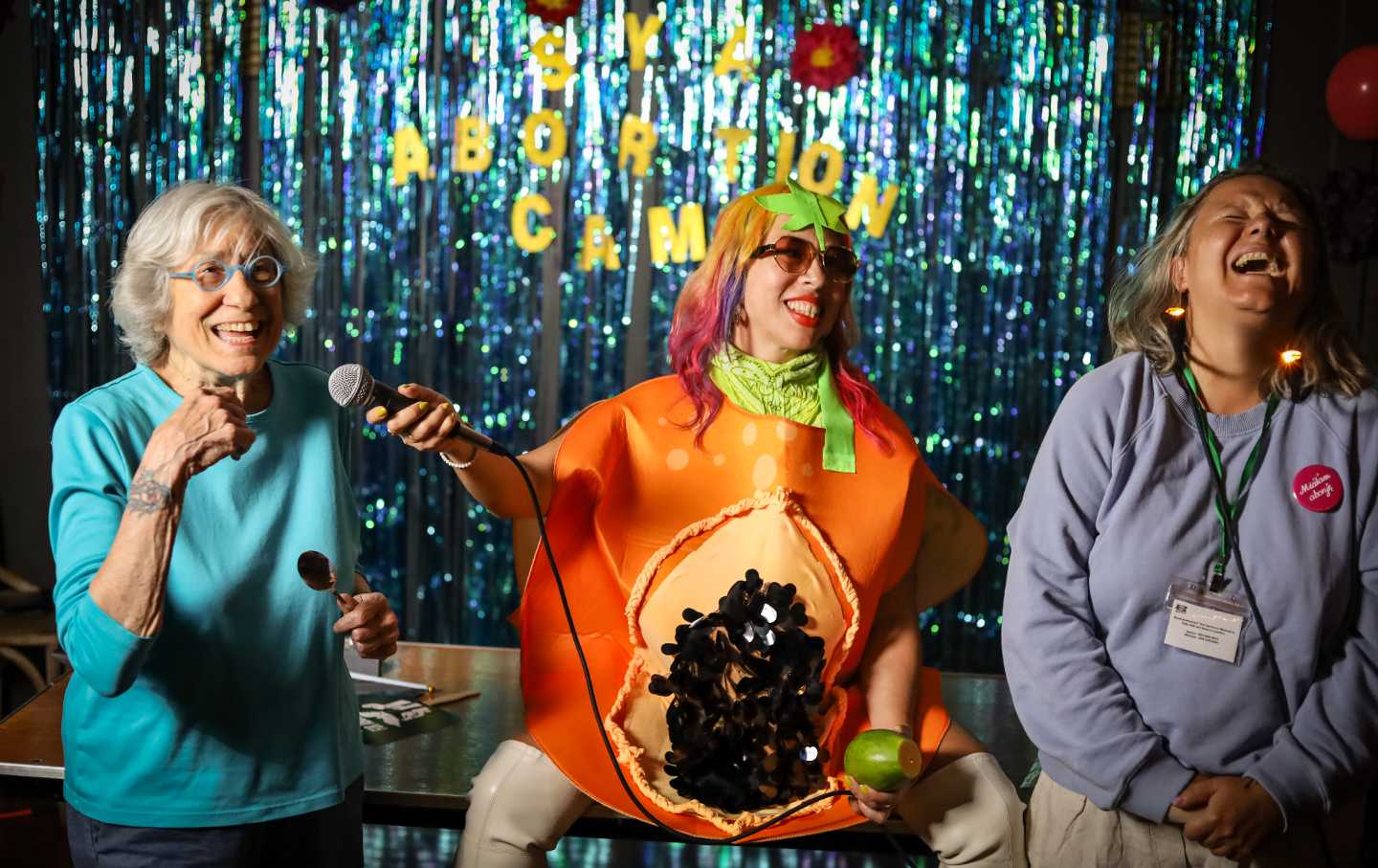 Three people standing at the front of a room in front of the letters