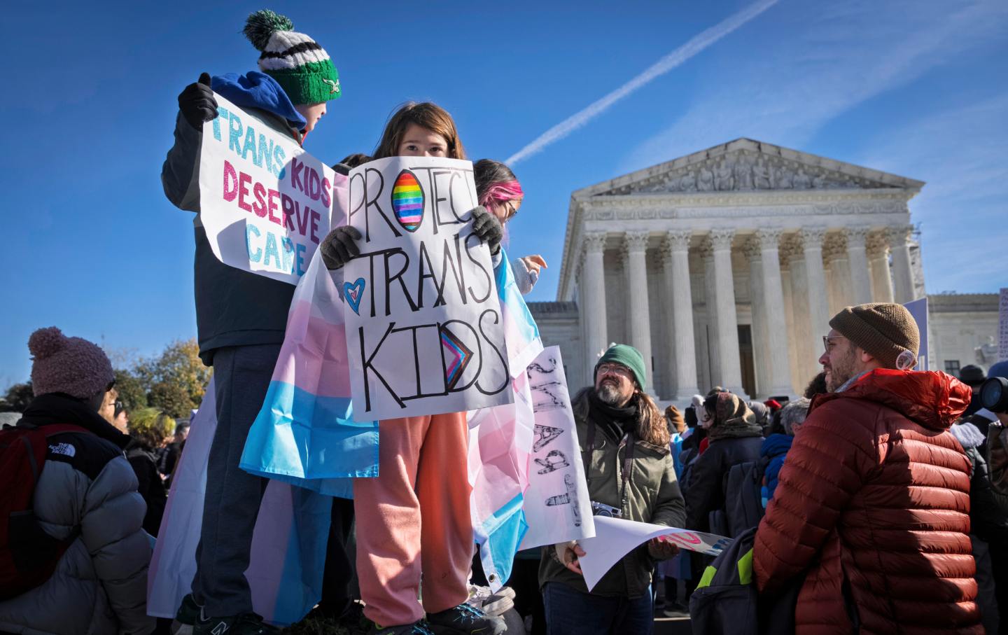Children hold signs and transgender pride flags as supporters of transgender rights rally by the Supreme Court, Dec. 4, 2024, in Washington.